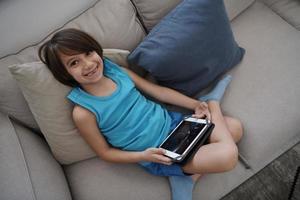 liten arab pojke Sammanträde på soffa och spelar spel på digital läsplatta foto