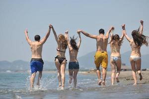 Lycklig människor grupp ha roligt och löpning på strand foto