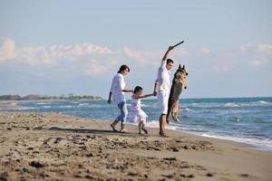 Lycklig familj spelar med hund på strand foto