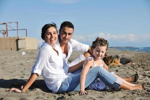 Lycklig familj spelar med hund på strand foto