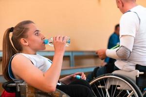 en kvinna rullstol basketboll spelare sitter i ett invlad rullstol på en ha sönder och drycker vatten. foto