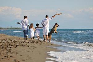 Lycklig familj spelar med hund på strand foto