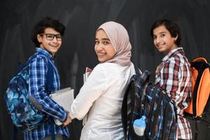 arabicum tonåringar, studenter grupp porträtt mot svart svarta tavlan bär ryggsäck och böcker i skola.selektiv fokus foto
