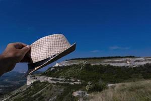 en hatt i de turisternas hand mot de bakgrund av en berg räckvidd och en blå himmel. resa begrepp. foto