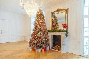 klassisk jul dekorerad interiör rum, ny år träd med röd och guld dekorationer. modern vit klassisk stil interiör design lägenhet med öppen spis och jul träd. jul eve på Hem. foto