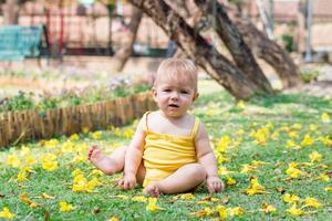 söt bebis flicka med blond hår är spelar på gräs med gul blommor på en solig dag i parkera. foto