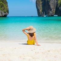 kvinna turist i gul baddräkt och hatt, glad resenär som solar på Maya Bay Beach på phi phi island, krabi, thailand. landmärke, destination sydostasien resor, semester och semester koncept foto