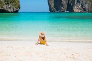 kvinna turist i gul baddräkt och hatt, glad resenär som solar på Maya Bay Beach på phi phi island, krabi, thailand. landmärke, destination sydostasien resor, semester och semester koncept foto