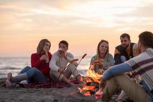 grupp av ung vänner Sammanträde förbi de brand på strand foto