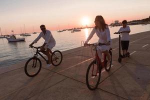 Lycklig familj njuter en skön morgon- förbi de hav tillsammans, föräldrar ridning en cykel och deras son ridning ett elektrisk skoter. selektiv fokus foto