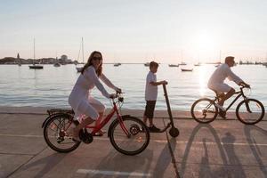 Lycklig familj njuter en skön morgon- förbi de hav tillsammans, föräldrar ridning en cykel och deras son ridning ett elektrisk skoter. selektiv fokus foto