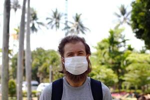 porträtt av europeisk man på en bakgrund av sommar tropisk parkera med medicinsk ansikte mask för skydda han själv från coronavirus sjukdom, influensa virus och Övrig infektioner. foto