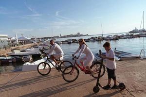 Lycklig familj njuter en skön morgon- förbi de hav tillsammans, föräldrar ridning en cykel och deras son ridning ett elektrisk skoter. selektiv fokus foto