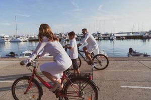 Lycklig familj njuter en skön morgon- förbi de hav tillsammans, föräldrar ridning en cykel och deras son ridning ett elektrisk skoter. selektiv fokus foto