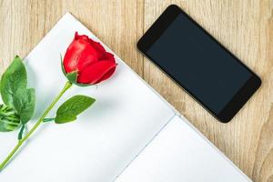 röd ro på tom anteckningsbok med smartphone valentine begrepp foto