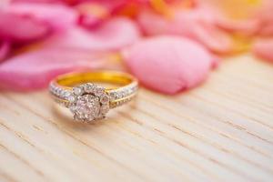 Smycken diamant ringa på trä tabell med skön rosa reste sig kronblad bakgrund stänga upp foto