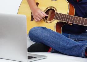 barn eller tonåring spelar akustisk gitarr använder sig av bärbar dator. inlärning och koppla av begrepp. foto