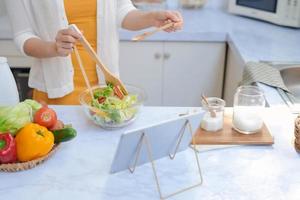 ämne skott av kvinna hand innehav rostfri stål kök tång med sallad löv ovan glas skål. foto