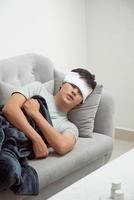 sjuk man liggande på soffa kontroll hans temperatur under en filt på Hem i de levande rum foto