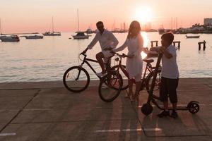 Lycklig familj njuter en skön morgon- förbi de hav tillsammans, föräldrar ridning en cykel och deras son ridning ett elektrisk skoter. selektiv fokus foto