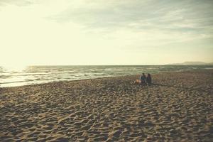 ung par Sammanträde på de strand bredvid lägereld dricka öl foto