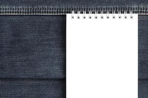 vit anteckningsbok med rena sidor liggande på mörk blå jeans bakgrund. bild med kopia Plats foto