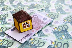 små leksak hus är lögner på en uppsättning av grön monetär valörer av 100 euro. en massa av pengar former ett oändlig högen foto