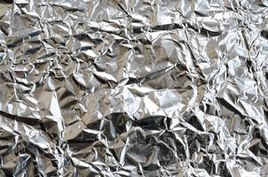 tunn rynkig ark av krossad tenn aluminium silver- folie bakgrund med skinande skrynkliga yta för textur foto