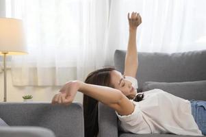 ung asiatisk kvinna tupplur på de soffa i levande rum , Lycklig friska livsstil begrepp foto