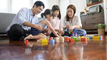 asiatisk familj med barn spelar och byggnad torn av färgrik trä- leksak block i levande rum på Hem, pedagogisk spel. foto