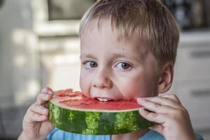 söt pojke äter vattenmelon på Hem. verklig känslor utan Framställ. foto