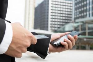 affärsman händer innehav kreditera kort och använder sig av telefon. uppkopplad handla inköp sälja eller betalning. foto