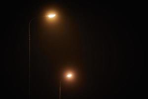 två natt lyktstolpe lyser med svag mystisk gul ljus genom kväll dimma på tyst natt foto