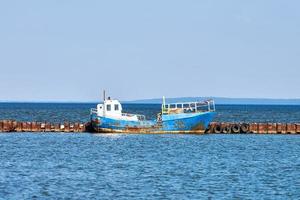 rostig gammal övergiven fiske båt förtöjd till rostig pir, förstört riden fiske trålare på hav foto