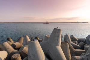 bogserbåt som seglar i havet för att bogsera fartyget till hamn. tetrapod vågbrytare i hamnen. vacker solnedgång över piren. foto