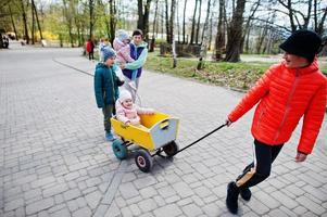 mamma med fyra barn som upptäcker och tittar på djur i djurparken. pojke drar trävagn. foto