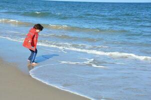 pojke i röd jacka och strand med vatten och sand foto