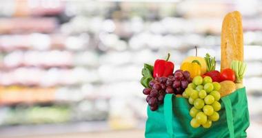 färska frukter och grönsaker i återanvändbar grön shoppingpåse med snabbköp livsmedelsbutik suddig ofokuserad bakgrund med bokeh ljus foto