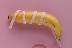 gul banan insvept i mäta tejp. män penis storlek begrepp. isolerat på rosa bakgrund foto