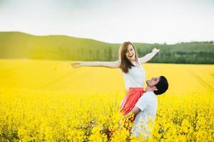 jag känner mig fri glad ung kvinna höjer händerna på mans händer, poserar tillsammans på gult blomfält under soligt sommarväder. romantiska par har kul utomhus. relationer koncept. foto