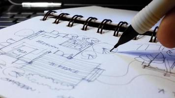 arkitektens händer är skiss arkitektonisk planer med pennor på en skissbok på en skrivbord med en bärbar dator. foto