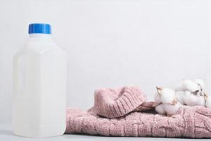ull rengöringsmedel i en flaska och rosa pullover med bomull knoppar. särskild tvättning lösning för mjuk delikat textil- och stickat kläder. foto