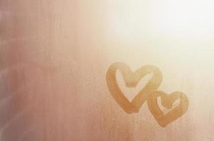 par av abstrakt suddig kärlek hjärta symbol dragen förbi hand på de våt fönster glas med solljus bakgrund. mall för valentine dag vykort foto