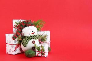 jul fortfarande liv med snögubbe och gåva lådor insvept av vit-grå papper med röd vit band på en röd bakgrund, dekorerad av gran grenar. jul och ny år begrepp med kopia Plats. foto