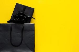 en svart gåva låda sätter i svart handla väska med gul bakgrund. svart fredag och boxning dag begrepp. foto