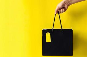 hand innehav svart handla väska med tom gul pris märka med gul bakgrund för svart fredag handla försäljning begrepp. foto