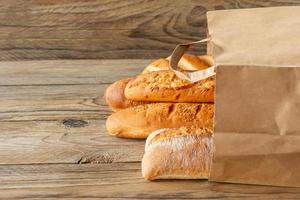 anordnad franska baguetter i papper väska och vete på rustik trä- bordsskiva foto