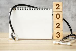2023 gott nytt år för hälsovård, försäkring, välbefinnande och medicinskt koncept. stetoskop och tom anteckningsbok för kopieringsutrymme din text foto
