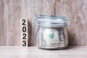 2023 Lycklig ny år med oss dollar pengar glas amerikan på trä tabell bakgrund. företag, investering, pensionering planera, finansiera, sparande och ny år upplösning begrepp foto