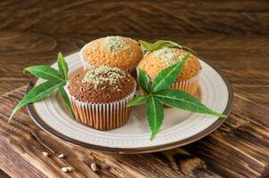 friska och gott vegan och gluten fri muffins toppade med hampa frön på en vit tallrik på trä- tabell. marijuana muffin muffins med cannabis löv foto